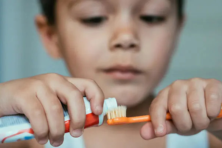 kid putting toothpaste in his toothbrush