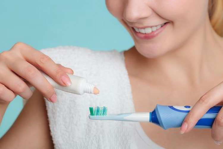 lady holding an electric toothbrush and toothpaste
