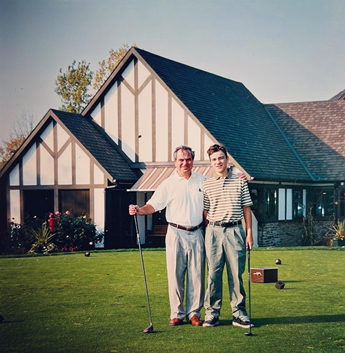 a picture of a father and his son carrying golf clubs with a house in the distance